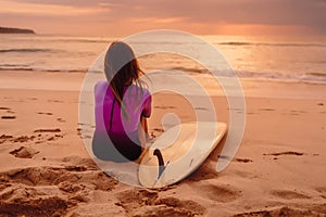 Surfer woman posing with surfboard on the beach at sunset