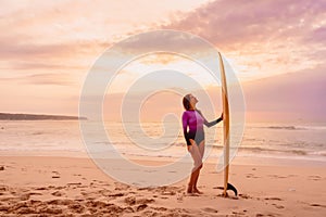 Surfer woman posing with surfboard on the beach at sunset