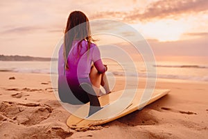Surfer woman posing with surfboard on the beach at sunset