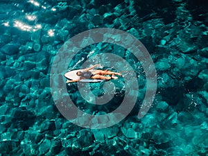 Surfer woman rowing on surfboard in turquoise ocean. Aerial view with surfgirl