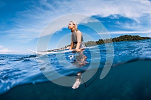 Surfer woman sit on surfboard and waiting wave in sea