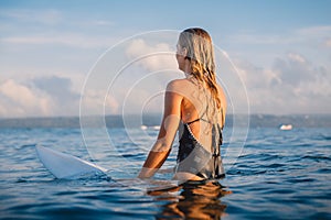 Surfer woman sitting on surfboard and wait waves. Woman with surfboard in ocean