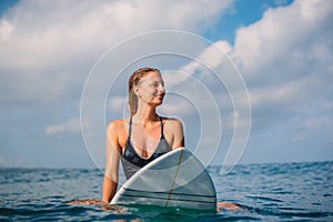 Surfer woman sitting on surfboard and wait waves. Woman with surfboard in ocean