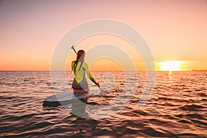 Surfer woman on stand up paddle board at quiet sea with warm sunset colors. Relaxing on ocean