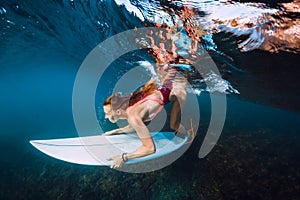 Surfer woman with surf board dive underwater with under big ocean wave