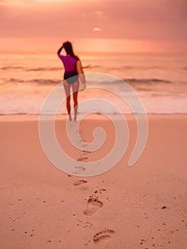 Surfer woman with surfboard on beach at sunset