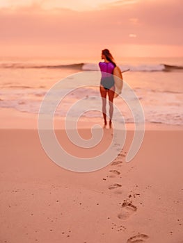 Surfer woman with surfboard on beach at sunset or sunrise