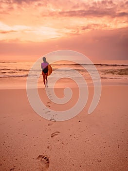 Surfer woman with surfboard on beach at sunset or sunrise