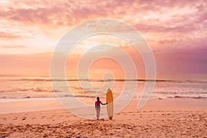 Surfer woman with surfboard on beach at sunset or sunrise