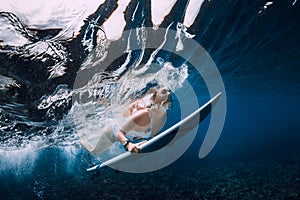Surfer woman with surfboard dive under wave in ocean