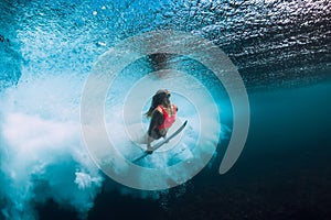 Surfer woman with surfboard dive underwater with under ocean wave.