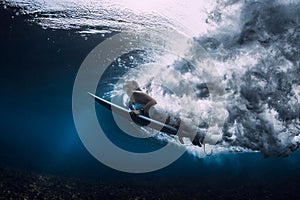 Surfer woman with surfboard duck dive under wave in tropical ocean