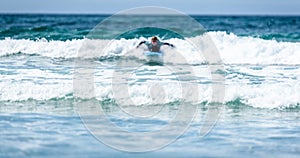 Surfer woman with surfboard is paddling on the wave.