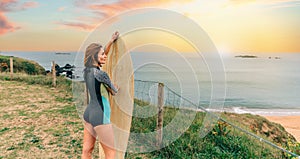 Surfer woman with wetsuit posing with surfboard looking at the beach