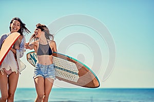 Surfers on beach having fun in summer. Young girls with a surf b