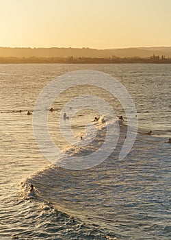 Surfers catching a wave in a calm sea in Byron Bay, Australia, on a beautiful sunset afternoon