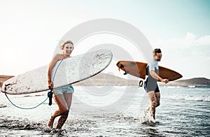 Surfers couple running together with surfboards on the beach at sunset - Sporty friends having fun going to surf