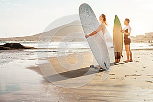 Surfers couple waiting for the high waves on beach - Sporty people with surf boards at sunset - Extreme sport and vacation concept