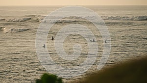 Surfers paddle out to catch waves at dawn. Group rides ocean swells, balances on boards. Watersport enthusiasts enjoy