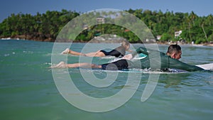 Surfers in swimwear paddling on surfboards. Man, woman in swimsuit swim on shore after session. Couple in love goes from