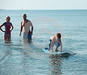 Surfers and their son are going to surf in the ocean in a sunny day