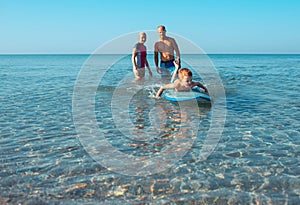 Surfers and their son are going to surf in the ocean in a sunny day