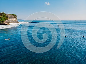 Surfers in tropical ocean at Bali island. Aerial view of rocky coastline with wave