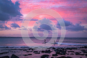 Surfers on waves in ocean under colorful sky