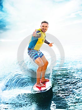 Surfing, blue ocean. Young Man show thumbs up on wakeboard.