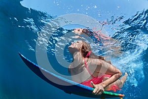 Surfing girl with board dive under ocean wave