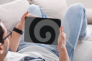 Surfing the internet. Man with smartwatch on couch at home and holds tablet with blank screen