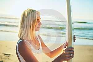 Surfing is a lifestyle. an attractive young woman standing in a swimsuit holding a surfboard on the beach.