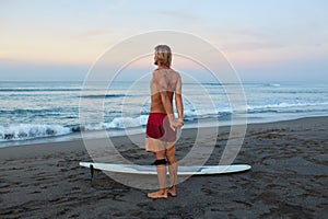Surfing Man. Stretching Surfer On Sandy Beach Going To Surf On Surfboard In Beautiful Tropical Ocean.