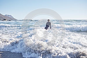 Surfing, man and swimming in sea waves, ocean and summer on blue sky in Cape Town, South Africa. Surfer guy, board and