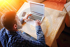 Surfing the net in office. Confident young man working on laptop and smiling while sitting at his working place in office