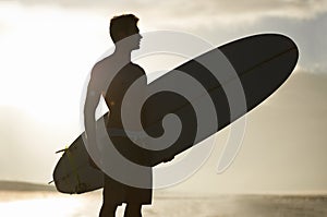 Surfing, sunset and silhouette of man at a beach with surfboard for freedom, travel or sports outdoor. Ocean, training