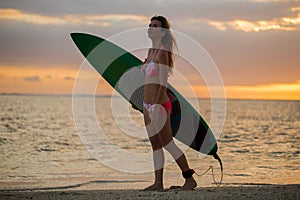 Surfing surfer girl looking at ocean beach sunset. Silhouette of female bikini woman looking at water with standing with