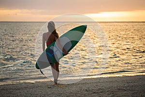 Surfing surfer girl looking at ocean beach sunset. Silhouette of female bikini woman looking at water with standing with