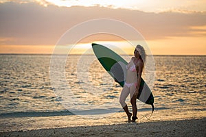 Surfing surfer girl looking at ocean beach sunset. Silhouette of female bikini woman looking at water with standing with