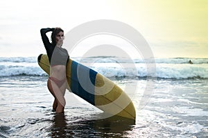 Surfing surfer woman babe beach fun at sunset. Girl on the beach in sunshine in warm evening sun holding blue surfboard