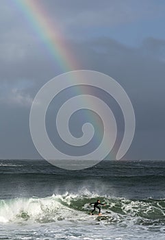 Surfing the waves. Surfer riding wave with rainbow on storm sky background