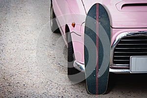 Surfskate with pink vintage car on road in the parking