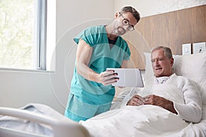 Surgeon With Digital Tablet Visiting Senior Male Patient In Hospital Bed In Geriatric Unit