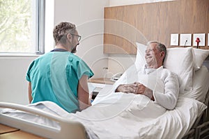 Surgeon With Digital Tablet Visiting Senior Male Patient In Hospital Bed In Geriatric Unit photo