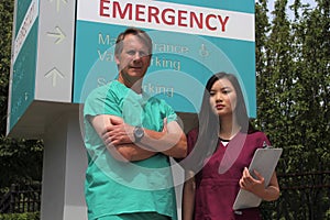 Surgeon or Doctor or Physician or Clinician and Asian Nurse Stand in Front of Hospital Emergency Room Sign