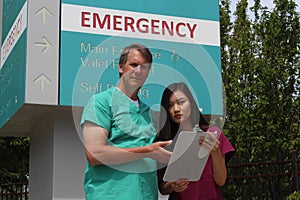 Surgeon, Doctor, Physician, Clinician and Asian Nurse Wearing Scrubs Stand in Front of Hospital Emergency Room Sign