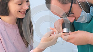 Surgeon examines wart on finger using dermatoscope magnifier before removing.