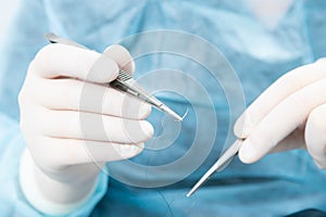 Surgeon holding a surgical needle holder with silk thread. Close-up