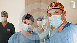 Surgeon male healthcare professional in a hospital operating theatre wearing a surgical cap and mask. Female doctor in