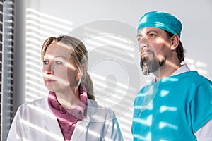 surgeon and nurse standing at a window, sun reflections